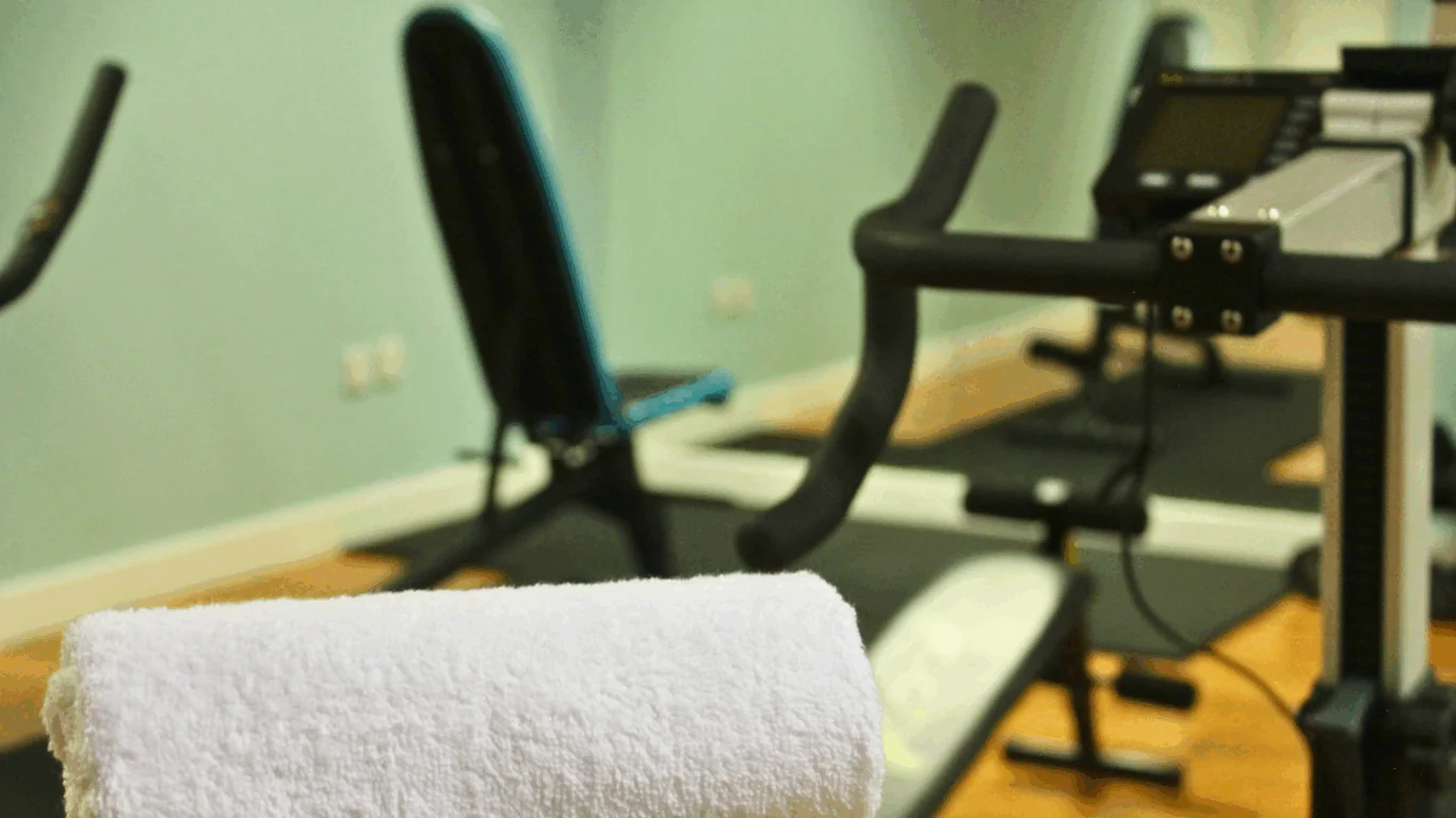 A close-up of a rolled white towel on gym equipment, with exercise machines and benches in the background.