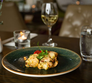 Elegant dining setup at Louis Fitzgerald Hotel with delicious appetiser, wine, and candlelit ambience.