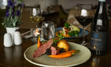 Elegant dining table with gourmet dish, wine, and soft lighting at Louis Fitzgerald Hotel.