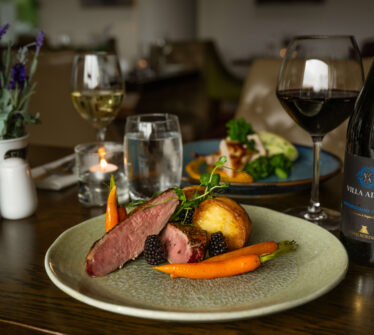 Elegant dining table with gourmet dish, wine, and soft lighting at Louis Fitzgerald Hotel.