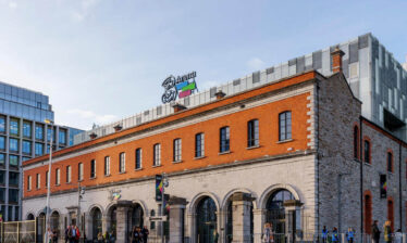 People walking by the historic Three Arena building on a sunny day in Dublin.