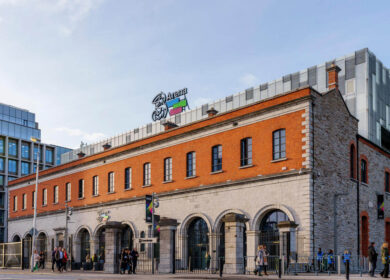 People walking by the historic Three Arena building on a sunny day in Dublin.