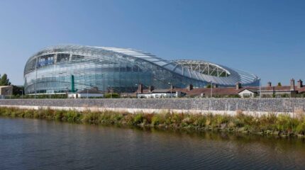 Modern glass architecture of Aviva Stadium in Dublin, with clear blue sky above.