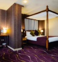 Elegant hotel room with a four-poster bed, modern decor, and warm lighting at Louis Fitzgerald Hotel.