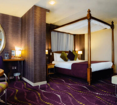 Elegant hotel room with a four-poster bed, modern decor, and warm lighting at Louis Fitzgerald Hotel.