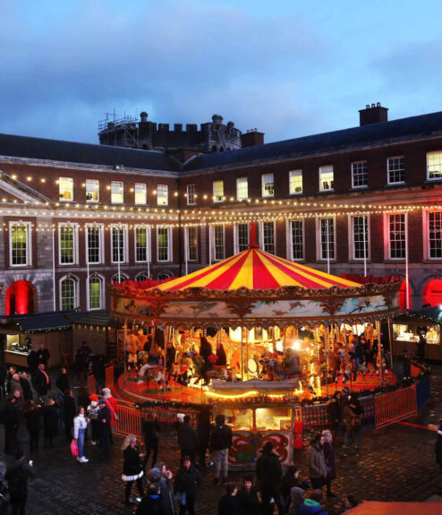 Festive courtyard with carousel, people enjoying Christmas market at evening.