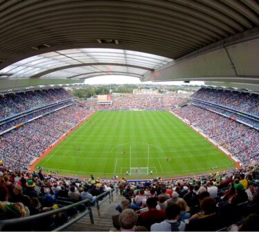 A packed stadium in Dublin hosts a lively match, surrounded by cheering fans under a semi-covered roof.