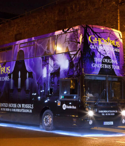 A vibrant, purple-lit ghost tour bus parked on a dimly lit Dublin street at night.