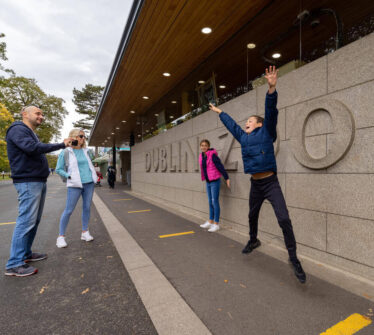 Family having fun outside Dublin Zoo entrance, with a child jumping joyfully.