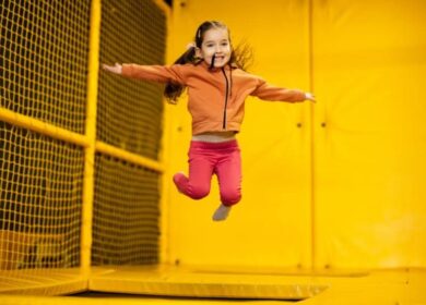 A joyful child jumps on a trampoline in an indoor play area with bright yellow walls.