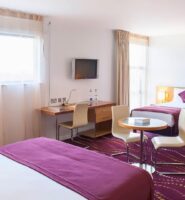 Spacious hotel room with three beds, vibrant purple decor, and a large window.