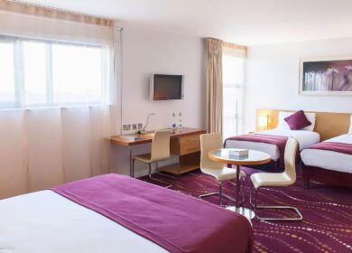 Spacious hotel room with three beds, vibrant purple decor, and a large window.