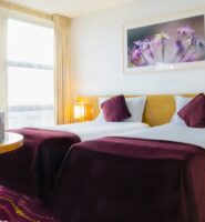 Elegant twin room at Louis Fitzgerald Hotel with plush bedding, vibrant decor, and large window.