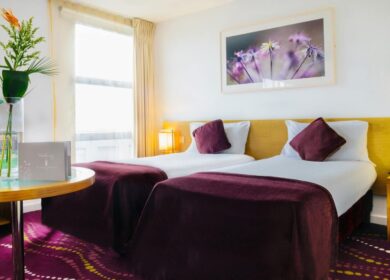 Elegant twin room at Louis Fitzgerald Hotel with plush bedding, vibrant decor, and large window.