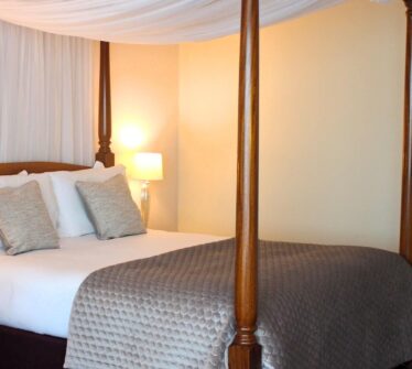 Elegant four-poster bed in a luxurious hotel room with soft lighting.