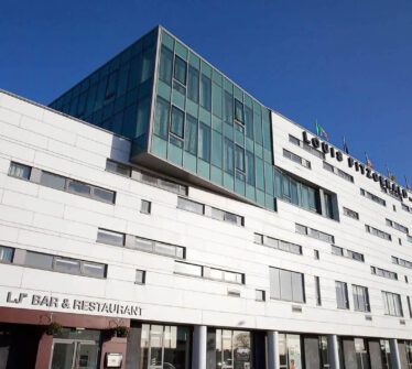 Modern exterior of Louis Fitzgerald Hotel with flags and clear blue sky.
