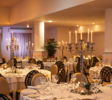 Elegant dining room with round tables, candelabras, and soft lighting in a warm, inviting setting.