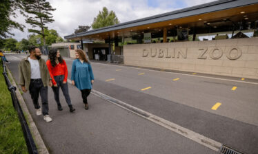 Three friends walking by Dublin Zoo entrance with lush greenery around.