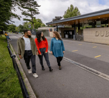 Three friends walking by Dublin Zoo entrance with lush greenery around.