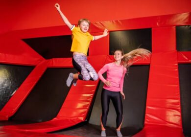 Child and woman joyfully jumping on trampolines in a vibrant red, family-friendly setting.