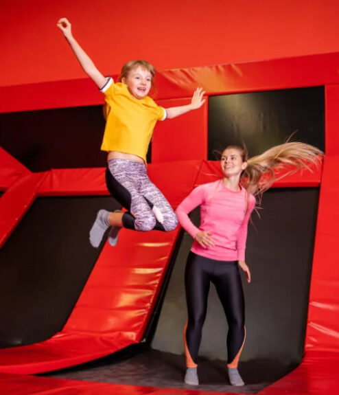 Child and woman joyfully jumping on trampolines in a vibrant red, family-friendly setting.
