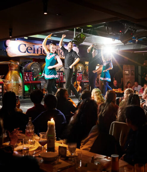Traditional Irish dancers perform on stage in a lively Dublin hotel bar, with an engaged audience.