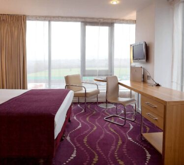 Elegant hotel room with a large bed, desk, and seating area by the window.