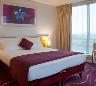 Elegant hotel room with a cosy double bed, stylish decor, and large window view at Louis Fitzgerald.