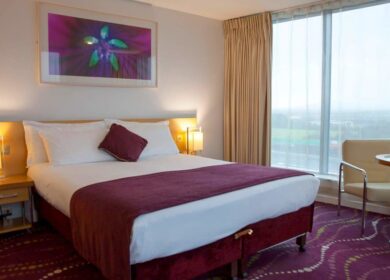 Elegant hotel room with a cosy double bed, stylish decor, and large window view at Louis Fitzgerald.