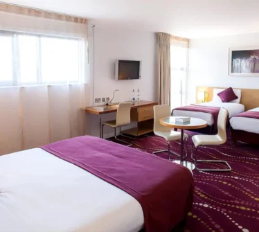 Spacious hotel room with three beds, purple accents, and a cosy seating area.
