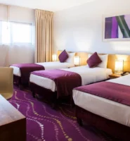 Cosy hotel room with three beds, purple decor, and welcoming atmosphere