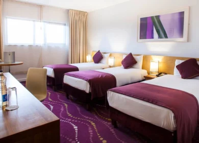 Cosy hotel room with three beds, purple decor, and welcoming atmosphere