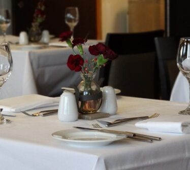 Elegant dining setup with wine glasses, white tablecloths, and a vase of red flowers at Louis Fitzgerald Hotel.