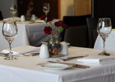 Elegant dining setup with wine glasses, white tablecloths, and a vase of red flowers at Louis Fitzgerald Hotel.