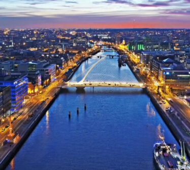 Vibrant Dublin sunset over River Liffey, city lights reflecting, calm waters, and bustling streets.