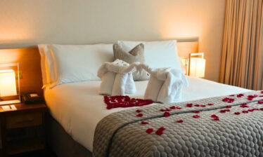 Elegant hotel room with swan towels and rose petals on a plush bed.