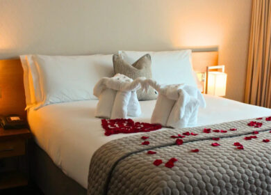 Elegant hotel room with swan towels and rose petals on a plush bed.