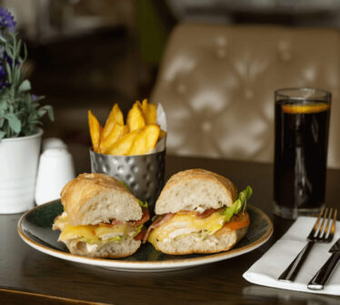 Gourmet sandwich with chips and drink on elegant hotel table setting.
