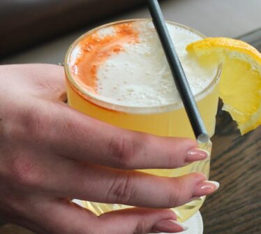 Hand holding a refreshing orange cocktail at the Louis Fitzgerald Hotel.
