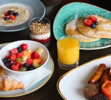 Assorted breakfast dishes with pancakes, fruit, pastries, and juice at Louis Fitzgerald Hotel.