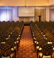 Elegant meeting room with rows of chairs and a projector screen at Louis Fitzgerald Hotel.