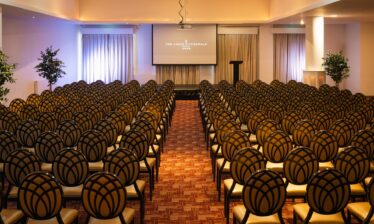 Elegant meeting room with rows of chairs and a projector screen at Louis Fitzgerald Hotel.