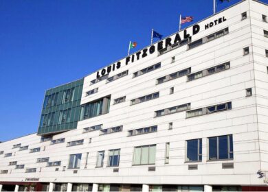 Modern facade of Louis Fitzgerald Hotel with flags under a clear blue sky.