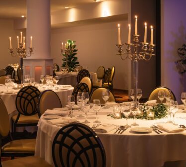 Elegant dining setup with round tables, white linens, and candlelit chandeliers at a hotel.