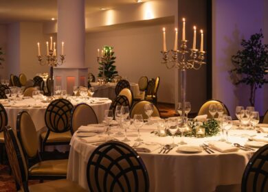 Elegant dining setup with round tables, white linens, and candlelit chandeliers at a hotel.