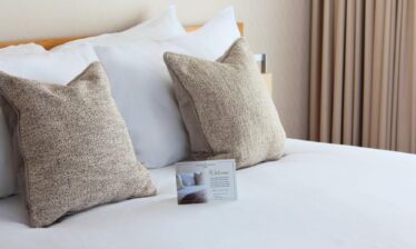 Elegant hotel bed with plush pillows and a welcome card at Louis Fitzgerald Hotel.