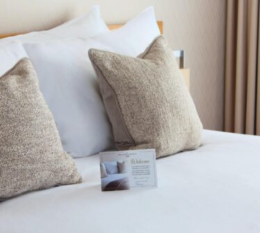 Elegant hotel bed with plush pillows and a welcome card at Louis Fitzgerald Hotel.