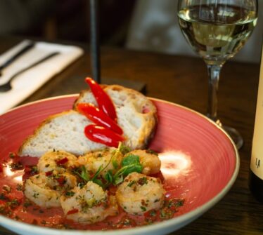 Elegant dining with shrimp, bread, roasted peppers, wine glass, and bottle at Louis Fitzgerald Hotel.