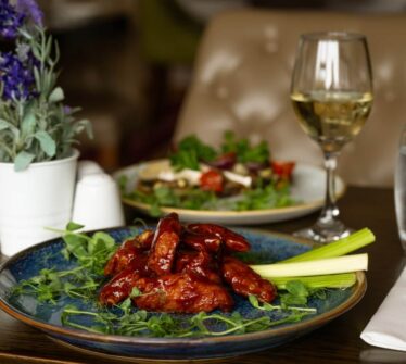 Elegant dining setup with a plate of glazed chicken wings, salad, wine, and water at a hotel restaurant.