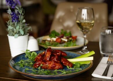 Elegant dining setup with a plate of glazed chicken wings, salad, wine, and water at a hotel restaurant.